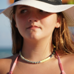 Purple & yellow Bermuda Triangle heishi choker on model wearing hat with a puzzled look on her face.