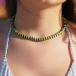 Electric Eel necklace of lime green & black heishi beads on model in blue & white striped swimsuit