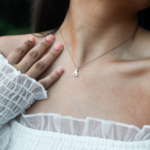 Lucky Feather Sailboat Necklace on neck of model in white shirt. Silver necklace with sailboat charm on nylon cord.