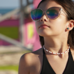 White seed bead choker necklace with red accent beads on model in sunglasses in front of pink and yellow lifeguard stand.