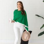 zestt organics Dreamsoft Travel Scarf Kelly Green Banded is green in color with white band & shown as shawl on smiling model in white shirt & pants holding a cup of coffee, rolling suitcase, & hat.