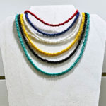 Sails collection of single strand seed bead necklaces displayed together on wooden display. All colors are shown, red, white, yellow, black, seafoam.