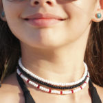 White Sail and Black Sail single strand seed bead necklace displayed on smiling model's neck along with Paradise Red seed bead necklace.