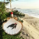 Santa's Sea Creatures Sea Turtle large seashell ornament with painted sea turtle in santa hat. Ornament is trimmed in gold leaf and hanging from christmas tree on beach.