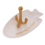 Hooked on You Ring Holder. White ceramic fish-shaped ring holder with gold-colored fishhook to hold rings. Message "Hooked on You" written in gold block letters on inside of dish. Displayed on white background.