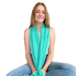 The Boho Shawl on smiling model sitting on the floor in jeans and white shirt in front of white background.