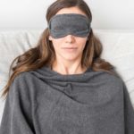 Travel Set Dark Gray on dark haired, smiling, sleeping model wearing blanket and eye mask.