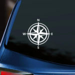 Compass Vinyl Decal white decal of compass rose with N E S W displayed on back window of blue car with dark tinting.