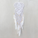 Heart Small Macrame Dreamcatcher displayed hanging against a light gray backdrop. Hoop on dreamcacher is white in color and heart shaped. Heart and tassels are white cotton macrame. Tassels are finished with white goose feathers.