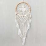 Mandala Large Macrame Dreamcatcher displayed hanging against a light gray backdrop. Hoop on dreamcacher is natural color rattan. Mandala and tassels are white cotton macrame. Tassels are finished with white goose feathers.