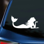 Mermaid Vinyl Decal white decal mermaid laying on stomach blowing kiss displayed on back window of blue car with dark tinting.