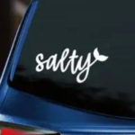 Salty Vinyl Decal white decal with script lettering and mermaid tail accent displayed on back window of blue car with dark tinting.