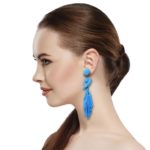 Blue Beaded Knot Post Statement Earrings shown on profile of model with brown hair in ponytail. Post earring is made with blue seed and bugle beads and is in a knot pattern with beaded fringe hanging down below the knot.