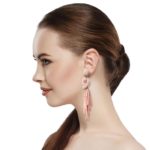 Coral Peach Beaded Post Statement Earrings shown on profile of model with brown hair in ponytail. Post earring is made with coral / peach seed and bugle beads and is in a knot pattern with beaded fringe hanging down below the knot.