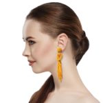 Orange Beaded Knot Post Statement Earrings shown on profile of model with brown hair in ponytail. Post earring is made with orange seed and bugle beads and is in a knot pattern with beaded fringe hanging down below the knot.