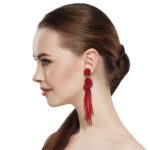 Red Beaded Knot Post Statement Earrings shown on profile of model with brown hair in ponytail. Post earring is made with red seed and bugle beads and is in a knot pattern with beaded fringe hanging down below the knot.